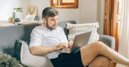 A man sitting on a couch while working from home with a laptop in his lap.