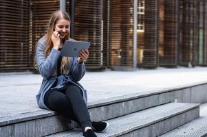 A woman sitting on steps outside using an iPad.