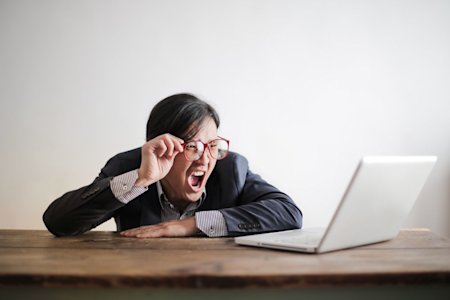 A person with a shocked, angry reaction while looking at their computer.