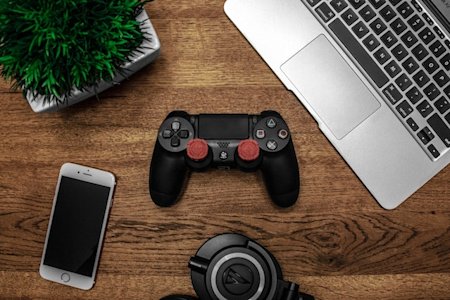 A gaming controller, laptop, and mobile device on a desk.