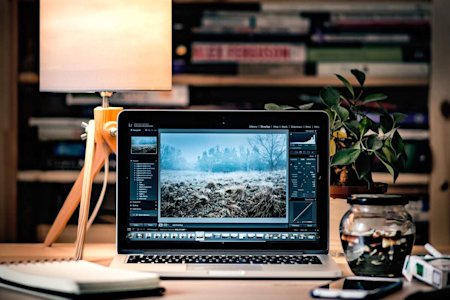 A Mac laptop displaying a photo editing software on a desktop in a library.