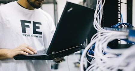 A field service technician working on a laptop near wires.