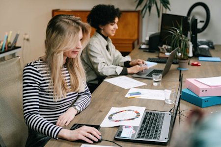 Two people working on their laptops on a conference table.