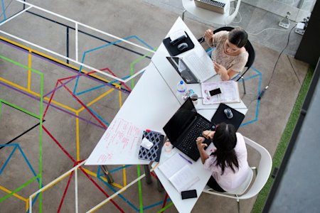 Two coworkers using their devices at a shared desk.