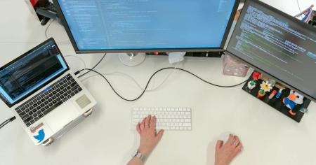 A person working at their desktop with a laptop and two monitors.
