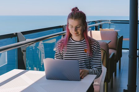 A woman working remotely outside near the ocean while using her laptop.