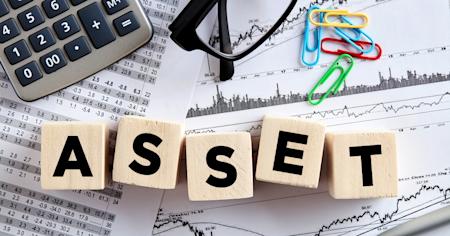 Blocks spelling 'ASSET' on top of financial charts, calculator, glasses, and paperclips.