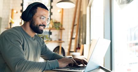 A man using a laptop and wearing headphones in a modern café, representing a seamless remote onboarding experience.