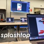 A classroom setting with laptops on tables and a large screen displaying digital artwork. The word splashtop is overlaid in white text at the bottom of the image.