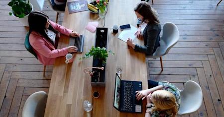 A group of workers on their laptops at a shared conference table.