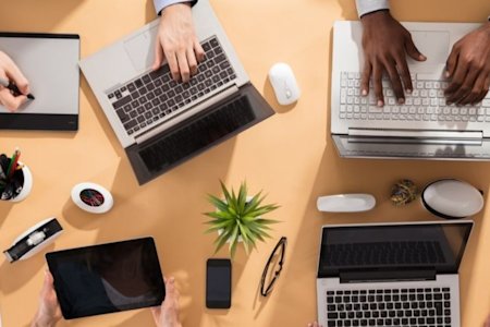 Team of people collaborating on laptops and tablets while sitting at a table