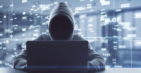 Person wearing a hood using a laptop to attempt to infiltrate networks as a hacker