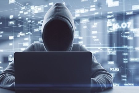 Person wearing a hood using a laptop to attempt to infiltrate networks as a hacker