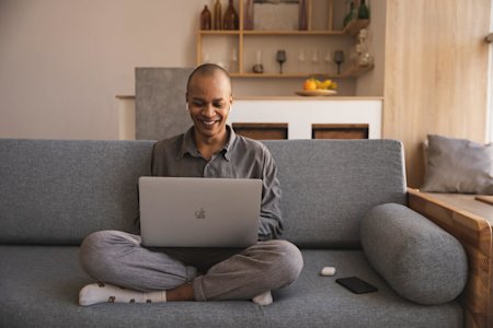 A man sitting on a couch in a living room on his laptop working from home and using Splashtop Enterprise