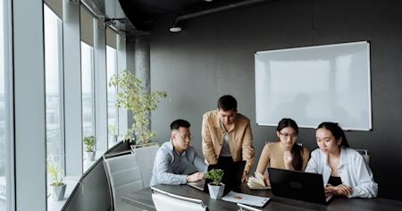 Coworkers in a meeting at a conference table with their computers.