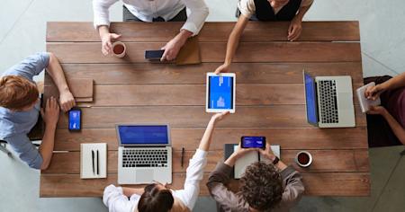 Co-workers sitting around a conference table using various devices.