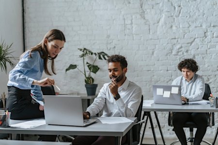 Two coworkers looking at a computer screen and talking to each other.
