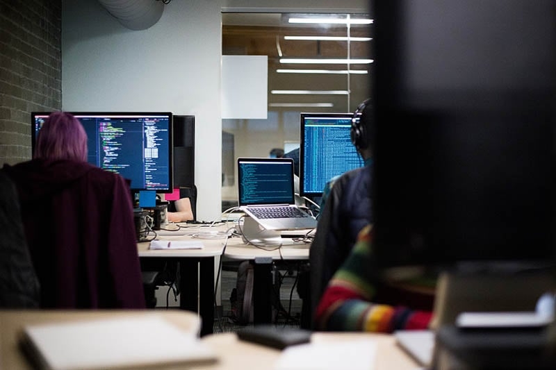 People sitting at computers with code on the screens