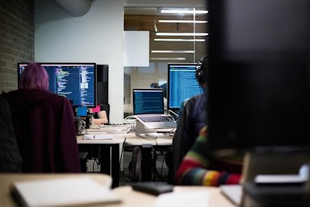 People sitting at computers with code on the screens