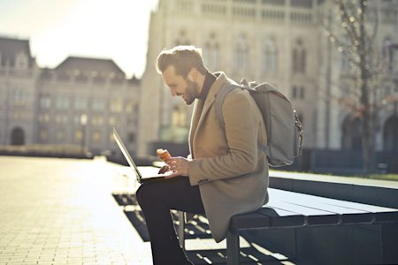 A man sitting outside and working remotely on a laptop.