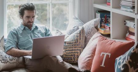 A man sitting on a couch at home working remotely from a laptop by using Splashtop.