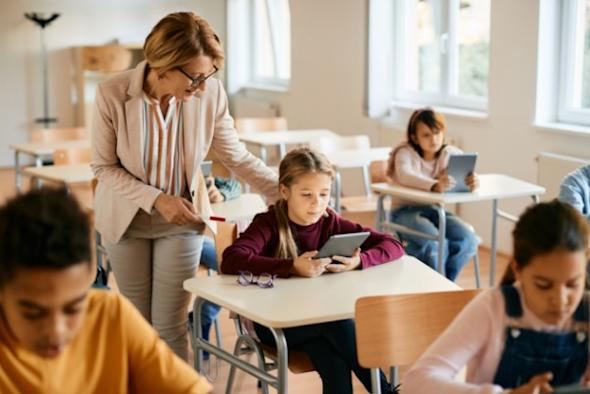 A teacher in front of a whiteboard, holding a tablet with Splashtop Whiteboard software displayed