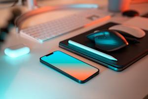 A smartphone, laptop, mouse, and keyboard sitting on a desk.
