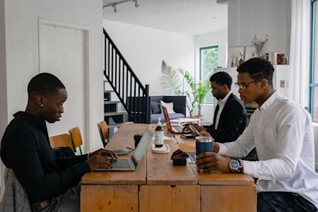 Three people working on their laptops on a shared tabled.