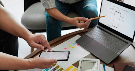 Two professionals collaborating on device management strategies with a laptop and smartphone, representing the efficiency of Autonomous Endpoint Management (AEM).