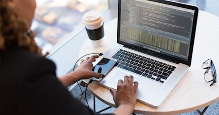 Woman coding on a laptop sitting at a coffee table.