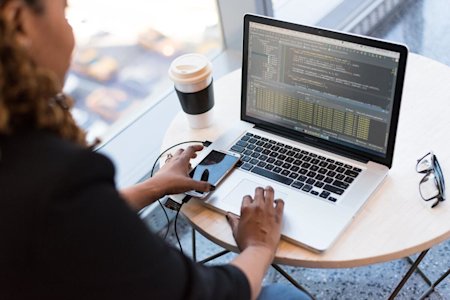 Woman coding on a laptop sitting at a coffee table.
