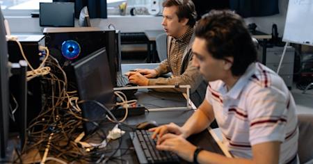 Two IT techs sitting at desks in an office and using computers.