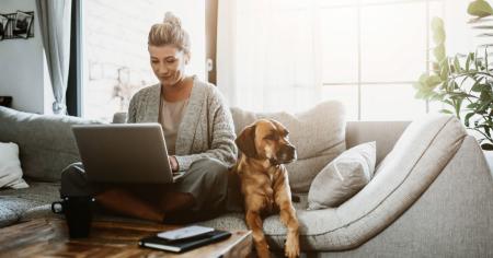 Female business owner, accompanied by her dog, using Splashtop's remote access to work from home on a couch during the pandemic