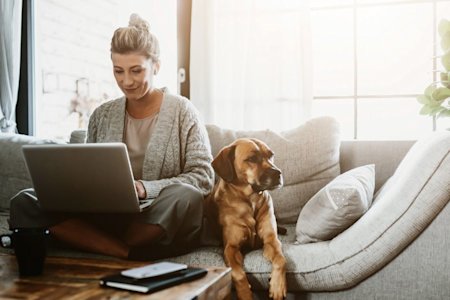Female business owner, accompanied by her dog, using Splashtop's remote access to work from home on a couch during the pandemic