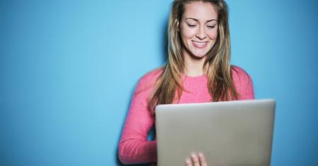 A woman smiling with her laptop in front of a blue background