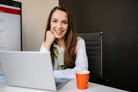 A woman smiling while working on a laptop.