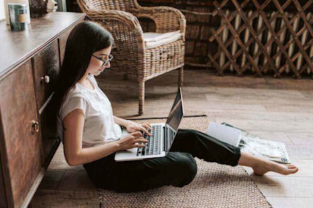A woman sitting on the floor using her laptop with Splashtop remote access software to work remotely.