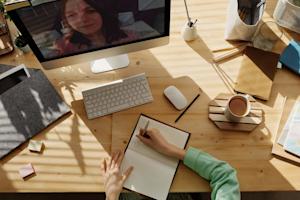 Writing in a notebook at a desk while looking at a computer