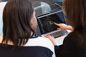 Two people looking at a laptop screen while working together.