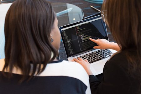 Two people looking at a laptop screen while working together.