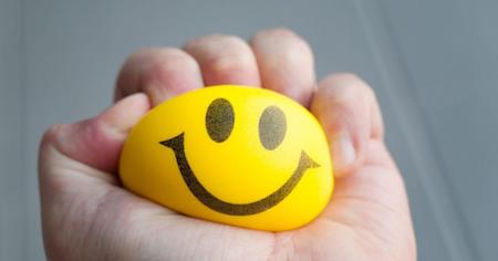 Stressed individual squeezing a stress ball with a happy face