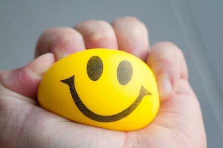 Stressed individual squeezing a stress ball with a happy face