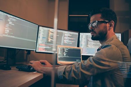 IT support at desk with a lot of computer screens displaying code on screen