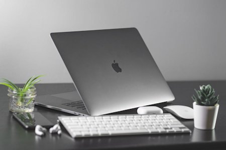 A Mac laptop, keyboard, mouse, and other items sitting on an office desk.