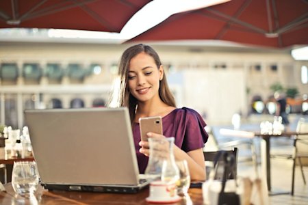 A happy woman working remotely at an outdoor restaurant by using Splashtop remote desktop software on her laptop.