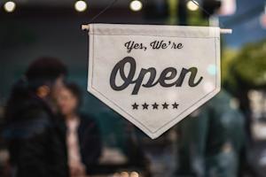 A sign saying "Yes, we're open" hanging in a small business's window.