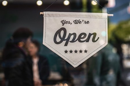 A sign saying "Yes, we're open" hanging in a small business's window.