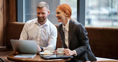 A man and woman working in a cafe looking at a laptop screen.