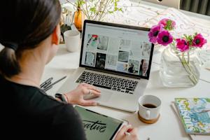 A graphic designer using a laptop and stylus tablet to create a design.