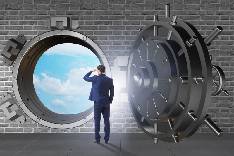 A man in a suit stands inside a large open vault, looking out at a bright sky with clouds through the circular opening in a brick wall.